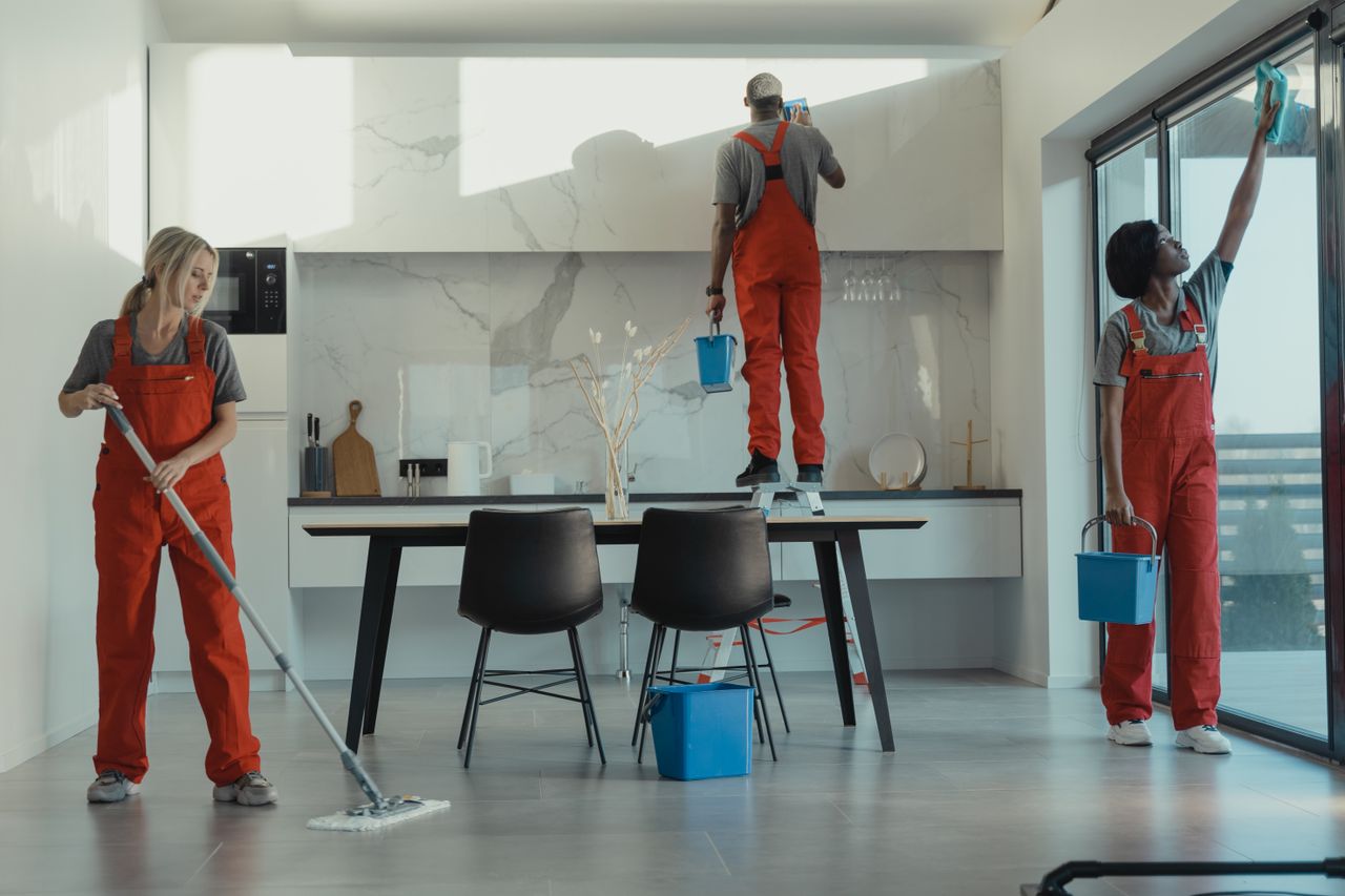 gallery-6 Group of cleaners in red uniforms mopping and wiping glass in a modern dining room.